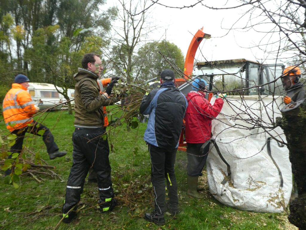 Rondom een big bag en een houtsnippermachine zijn vijf mensen bezig met snoeihout.